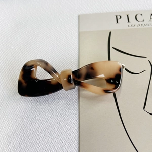 Detail showing high-end acetate tortoiseshell bow hair clip on a minimalist art card