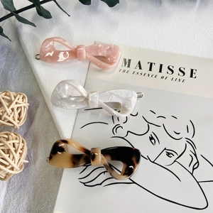 Close-up of three acetate bow hair clips in pink, white, and tortoise shell patterns