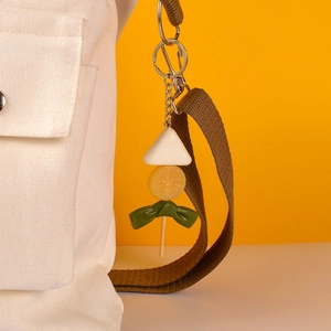 Realistic Oden skewer keychain charm hanging on a canvas bag strap with orange background
