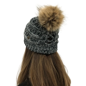 Detail view of cable knit beanie showing the cross strappy cutout back and pom pom