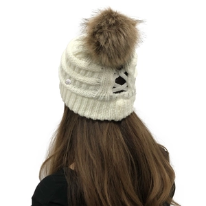 Detail of white knit beanie with a brown faux fur pom-pom and ponytail cross-opening