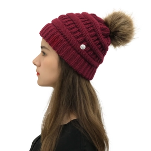 Detail view of burgundy knit beanie featuring a brown faux fur pom and rose metal charm