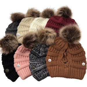 Detailed pile of knitted winter hats in various colors with large pom-poms and flower pins