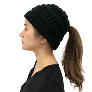 Detail of black ponytail knit beanie showing the functional hole for hair on a white background