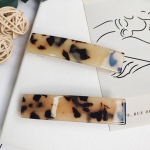 Detailed view of two acetate tortoise shell hair clips on a minimalist white canvas