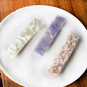 Three acetate hair clips with leopard and marble textures on a white ceramic plate