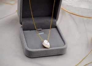 Detailed macro view of baroque pearl pendant with delicate golden chain in jewelry box