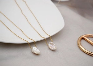 Close-up of white baroque pearl pendants on elegant gold chains over a ceramic plate