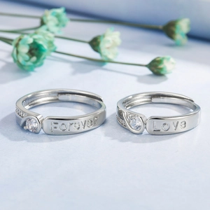 Silver heart-shaped couple rings engraved with Forever Love on light blue background