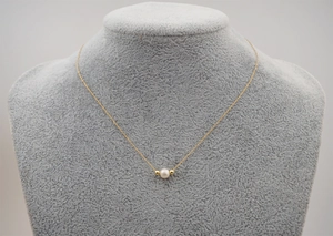 Close-up of a gold titanium chain with a freshwater pearl on a grey velvet mannequin