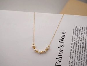 Close-up of a minimalist gold freshwater pearl necklace draped over a white book page