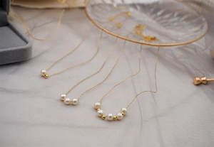 Detailed view of three gold titanium necklaces with varying freshwater pearl arrangements
