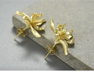 Macro shot of gold iris stud earrings with a brushed matte texture on a stone base