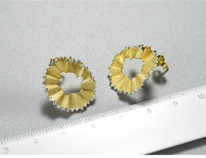 Macro detail of pencil shaving earrings in gold brushed metal and silver serrated edges