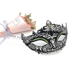 Detail of a black cutout metal masquerade mask with green rhinestones and floral accent