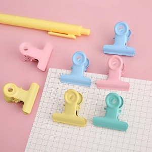 Creative macaron colored metal binder clips on pink background with stationery