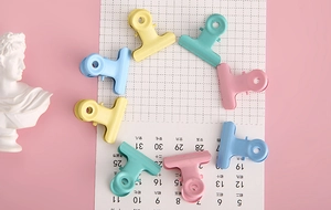 Macro shot of 8 candy-colored metal binder clips arranged in a circle on grid paper