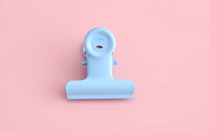 Close-up of a light blue matte metal bulldog clip on a soft pink background for stationery