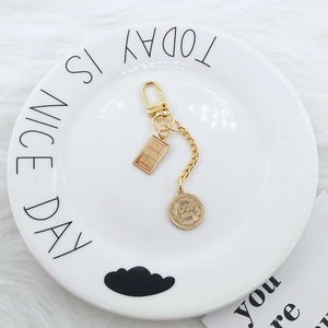 Detail of gold keychain with fine gold bar pendant and vintage coin charm on plate
