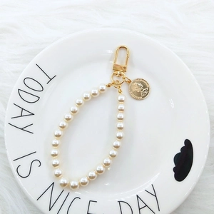 Detail of elegant pearl keychain with golden coin pendant and portrait embossing