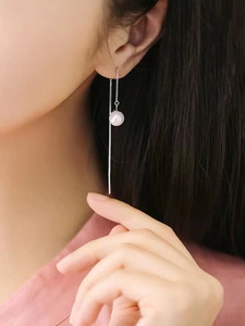 Detail of high-luster white pearl drop earrings with long silver chains on a model