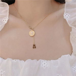 Detail of gold asymmetrical necklace featuring a white shell pendant and a hollow bear charm