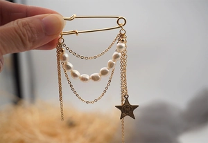 Detailed close-up of golden safety pin brooch with fresh water pearls and metal chains