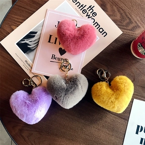 Cute heart-shaped plush keychains in pink, purple, grey, and yellow on a wooden table