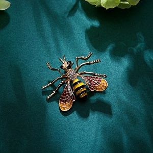 Close-up of golden honey bee brooch with rhinestones and orange enamel wings on green fabric