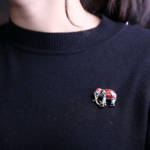 Detailed view of an elephant brooch with red enamel on a black sweater