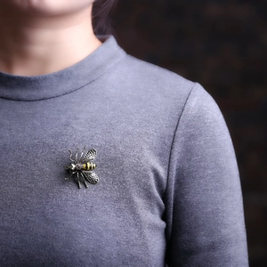Macro detail of a vintage bee brooch with textured wings on grey knitwear clothing