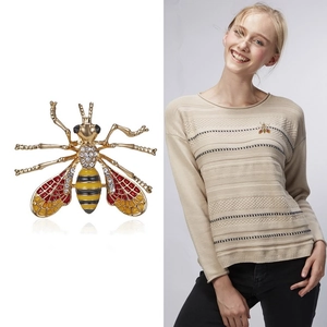 Detailed view of a golden bee brooch with red enamel wings and sparkling white crystals