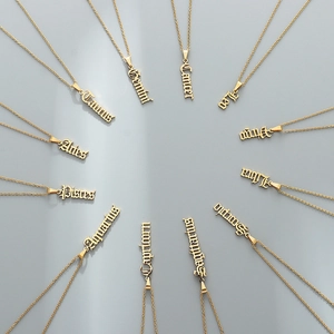 Set of 12 zodiac gold necklaces with Gothic font pendants on a gray background