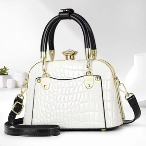 Close-up of white crocodile texture handbag with gold hardware and black tubular handles