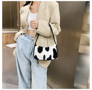 Detailed view of black and white cow print plush underarm bag worn by a model