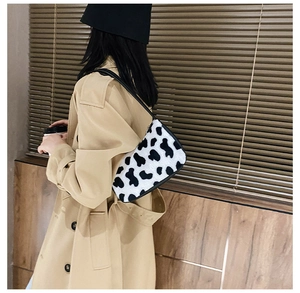 Close-up of zebra pattern plush shoulder bag worn by model against wood background