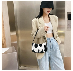 Chic cow print plush shoulder bag with black strap shown in a modern street style setting