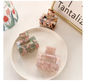 Three square acetate hair claws with marble and floral patterns shown in a stylish setting