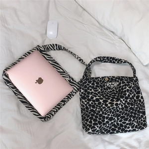 Detail of zebra and leopard print canvas tote bags holding a laptop on a white bed