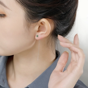 Model wearing silver drop earrings with a square green gemstone and long chain fringe