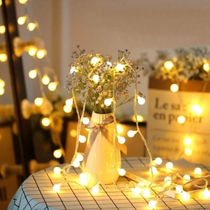 Detail of warm white LED globe string lights wrapped around a white ceramic vase