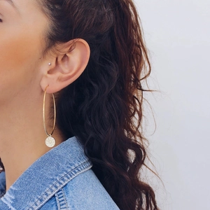 Detailed view of large gold hoop earring with a sparkling pavé circle pendant on a model