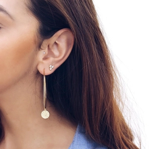 Close-up of gold hoop earring with round relief pendant and small crystal studs on ear