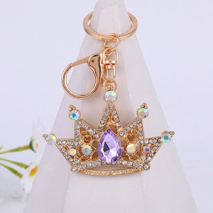 Golden crown keychain with purple and clear rhinestones on white display stand