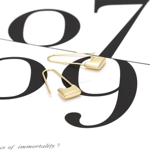 Minimalist gold-plated safety pin and lock earrings for women on a typography background