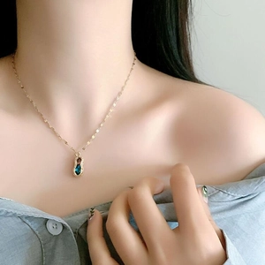 Close-up of golden peanut-shaped pendant necklace with gradient blue zircon on model