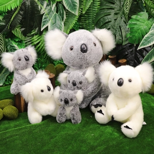 Peluche realistici di koala grigi e bianchi su uno sfondo di erba tropicale verde lussureggiante
