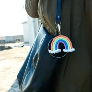 Détail d'un pendentif arc-en-ciel fait main en coton et perles de bois sur un sac en cuir