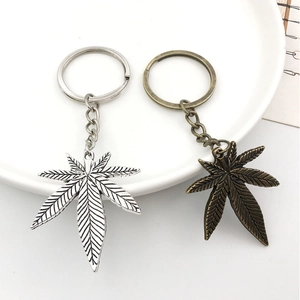 Detail of silver and bronze cannabis leaf metal keychains with chain on a white plate
