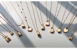 Flat lay of ten 18K gold plated stainless steel necklaces with heart and lock pendants